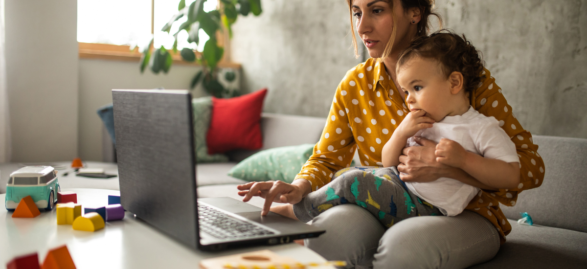 mother holding a baby while working on a laptop